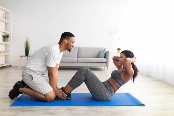 Seitenansicht eines jungen schwarzen Paares, das zu Hause gemeinsam Bauchmuskelübungen macht, Kopierraum - Foto, Bild