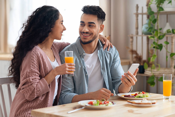 Šťastný mladý arabský pár pomocí Smartphone během snídaně v kuchyni - Fotografie, Obrázek