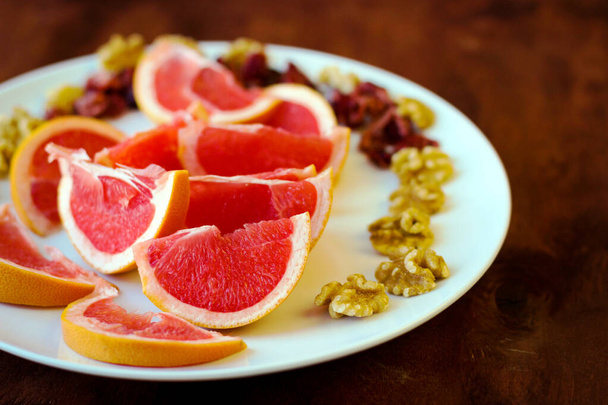 Wonderful vegan food: grapefruit sliced with slices, walnut kernels, dried cranberries stand on a white plate - Photo, Image