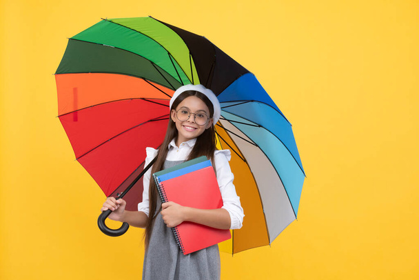 happy teen girl in glasses and beret under colorful umbrella for rain protection in autumn season hold notebook, school. - Photo, Image