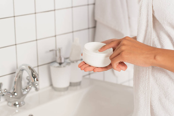 vista da vicino della giovane donna afroamericana che tocca la crema in vaso con il dito in bagno - Foto, immagini