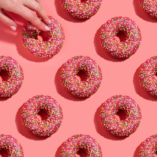 Donuts seamless pattern in glaze on pink background, with woman hand - Fotoğraf, Görsel