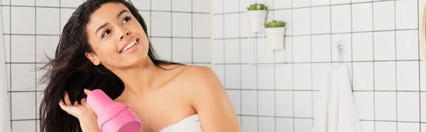 мечтательный молодой африканский американец женщина укладки волос с сушилкой рядом в ванной комнате, баннер - Фото, изображение