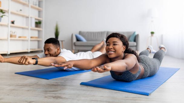 Home trainings during covid lockdown. Strong black couple exercising on sports mats, doing yoga or pilates indoors - Photo, Image