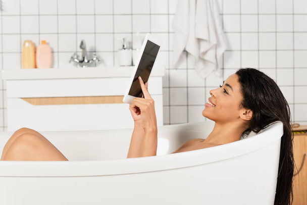 Genç Afrikalı Amerikalı kadın banyo yapıyor ve boş ekranlı dijital tablet kullanıyor. - Fotoğraf, Görsel