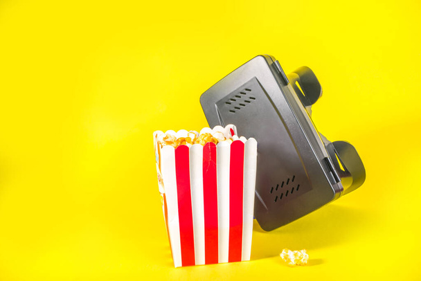 Okulary wirtualnej rzeczywistości z wiadrem popcornu, filmem VR i rozrywką w domu, na żółtym jasnym tle. - Zdjęcie, obraz