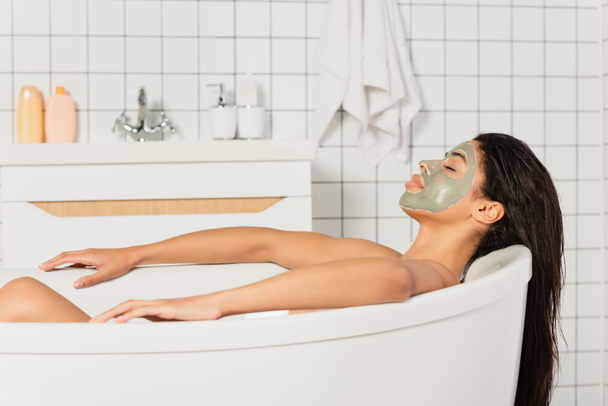 pacífico joven afroamericano mujer con máscara de barro en la cara tomando baño - Foto, Imagen