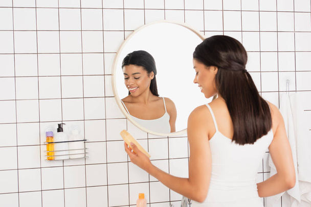 young african american woman holding shower gel near mirror in bathroom - Photo, Image