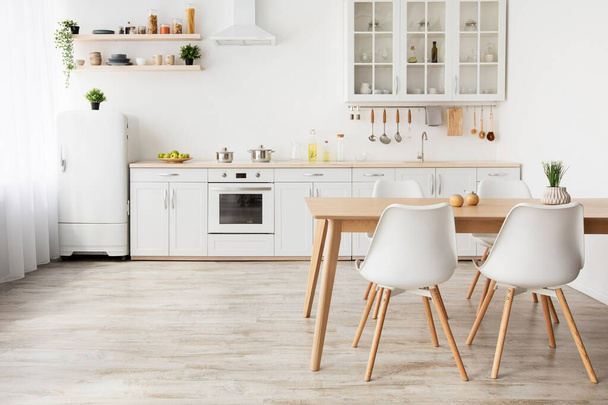 Легкий дизайн кухни в скандальном стиле. Деревянный обеденный стол и белая мебель, маленький холодильник, пустое место - Фото, изображение