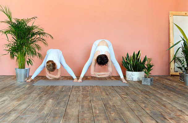 Mujer sonriente y niña practicando yoga mientras estoy de pie en la estera en la acogedora sala de estar con plantas - Foto, imagen