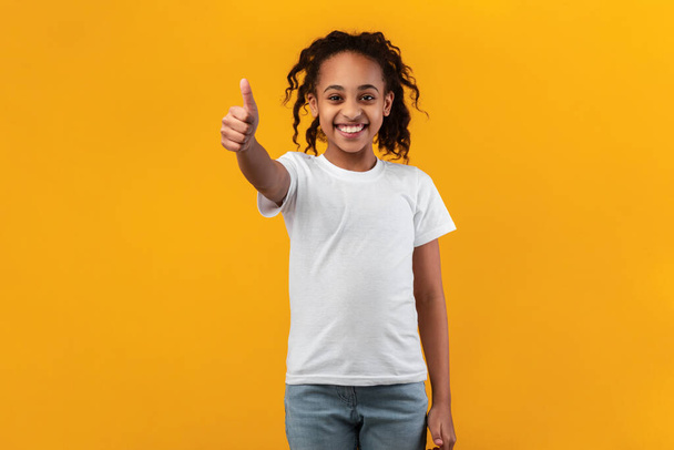 Ευτυχισμένο μαύρο κορίτσι που χύνει τους αντίχειρες και χαμογελά - Φωτογραφία, εικόνα