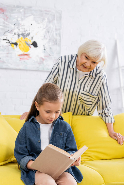 Kid reading book near blurred granny at home  - Foto, immagini
