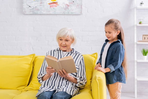 Großmutter liest Buch bei glücklichem Mädchen zu Hause  - Foto, Bild