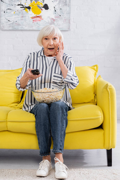 Excited woman with popcorn and remote controller watching tv  - Foto, Imagem