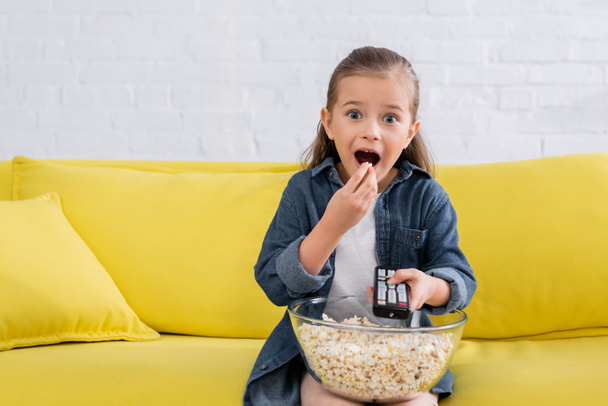 Aufgeregtes Mädchen mit Fernbedienung isst Popcorn  - Foto, Bild