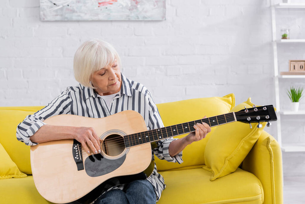 Senior vrouw speelt akoestische gitaar thuis  - Foto, afbeelding