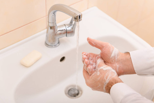 käsienpesu saippualla tai geelillä juoksevan veden alla pesualtaassa, puhtaus ja hygienia, miesten kädet pukeutunut valkoiseen paitaan - Valokuva, kuva