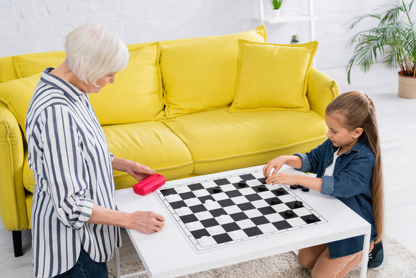 Child and grandparent playing checkers game on board  - Photo, Image