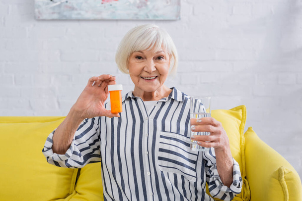 Senior vrouw met water en pillen glimlachen op de camera  - Foto, afbeelding