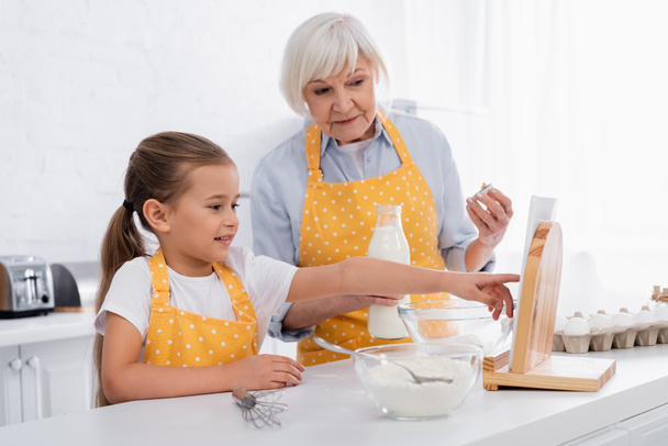 家庭で食材や祖母の近くのデジタルタブレットを使用して陽気な子供  - 写真・画像