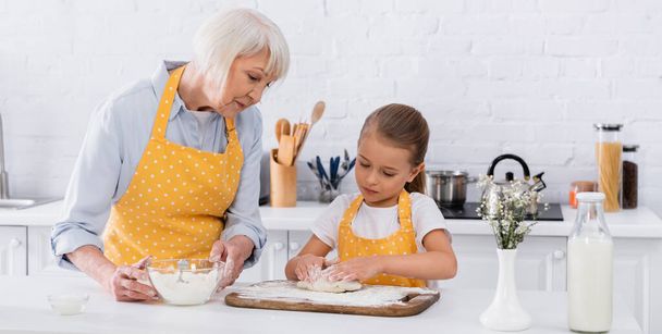 Kid making dough near granny in apron holding flour, banner  - 写真・画像