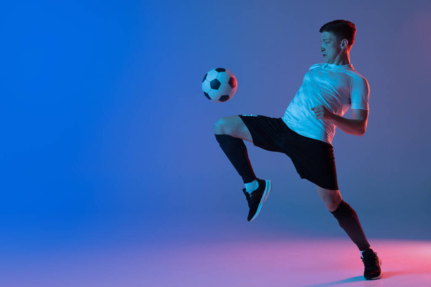 Young Caucasian man, male soccer football player training isolated on gradient blue pink background in neon light - Фото, зображення