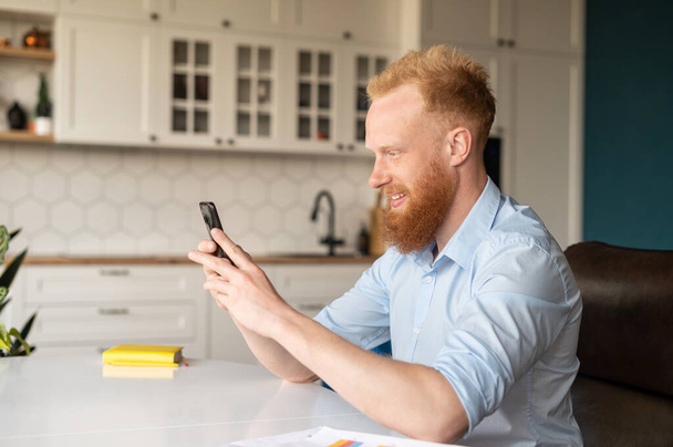 Side view of handsome red haired caucasian man using smartphone - Фото, зображення