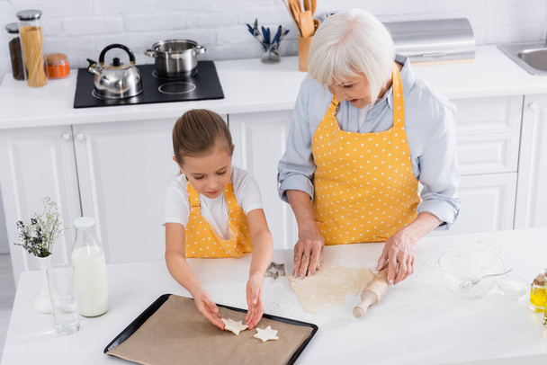 High angle view of child putting dough on baking sheet near granny with rolling pin  - Photo, Image