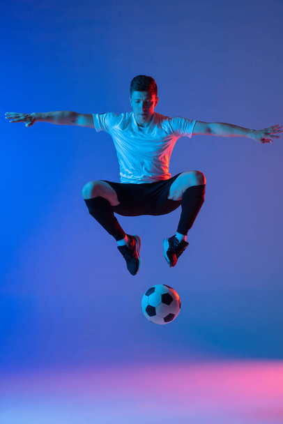 Young Caucasian man, male soccer football player training isolated on gradient blue pink background in neon light - Fotó, kép