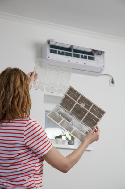 Vrouw vervangt oude stoffige luchtfilter door nieuwe op airconditioner. - Foto, afbeelding