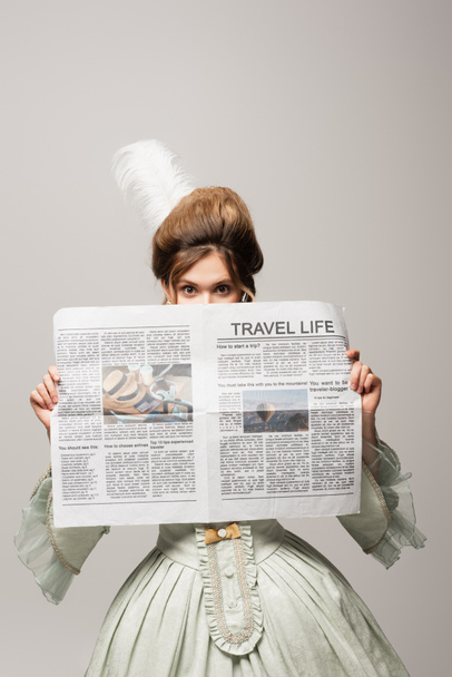 mujer de estilo retro oscurecer la cara con la vida de viaje periódico aislado en gris - Foto, imagen