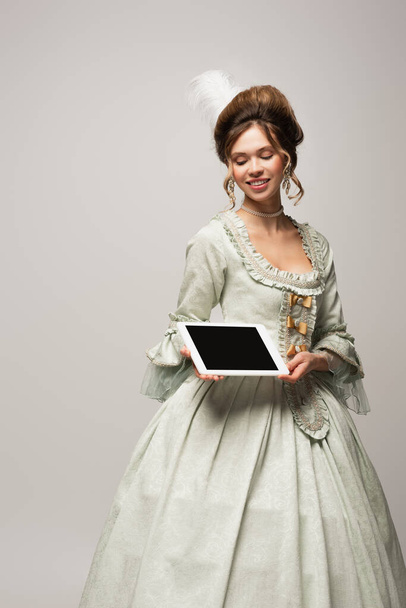 ευχαριστημένη γυναίκα σε ρετρό φόρεμα κρατώντας ψηφιακό δισκίο με λευκή οθόνη απομονωμένη σε γκρι - Φωτογραφία, εικόνα