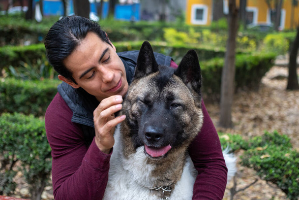 Mladý svalnatý hispánec drží a hladí své psy v parku - Fotografie, Obrázek