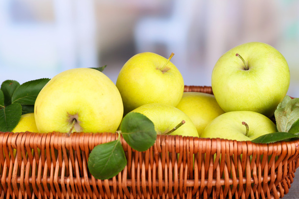 Ripe sweet apples with leaves in wicker basket on light background - Valokuva, kuva
