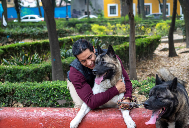 Young muscular hispanic man holding and petting his dogs in the park - Photo, Image