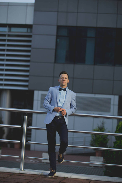 A young handsome elegant man in a blue suit and bow leaning on a railing - Photo, image