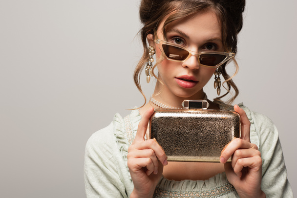 stylish woman in vintage outfit holding golden clutch bag isolated on grey - Fotoğraf, Görsel