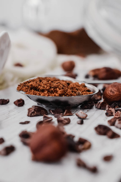 A vertical closeup shot of nuts, chocolate chips and a spoon of coffee on a kitchen table - Fotó, kép
