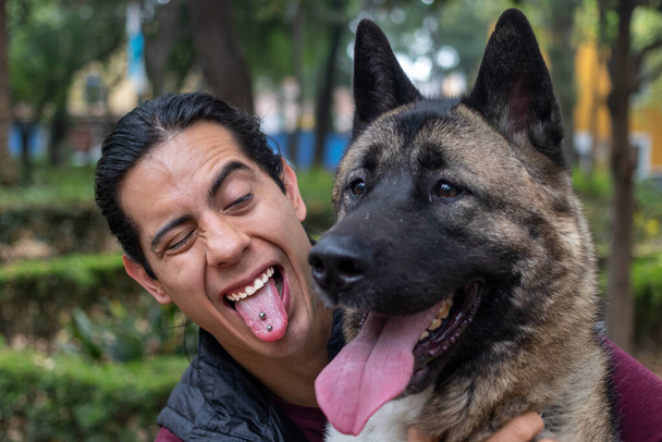 Young muscular hispanic man holding and petting his dogs in the park - Foto, Imagen