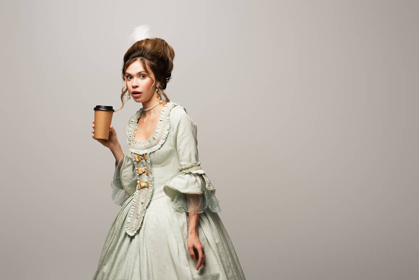 surprised woman in vintage outfit holding paper cup while looking at camera isolated on grey - Photo, Image