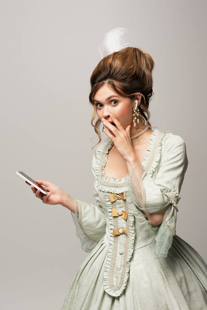 surprised vintage style woman holding smartphone and covering mouth with hand isolated on grey - Photo, Image