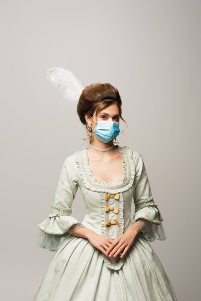 elegáns nő vintage ruha és orvosi maszk néz kamera elszigetelt szürke - Fotó, kép