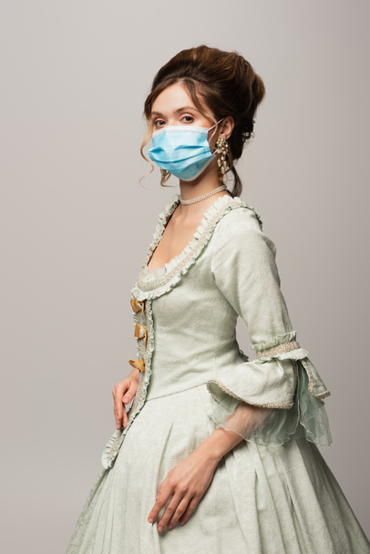 stylish woman in retro outfit and medical mask looking at camera isolated on grey - Photo, Image