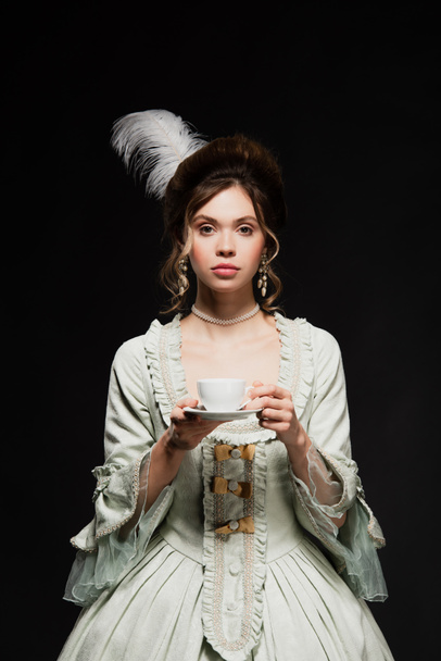 charming woman in vintage pastel grey dress holding cup of coffee isolated on black - 写真・画像