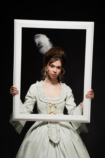 charming woman in elegant vintage outfit holding white framing isolated on black - Foto, immagini