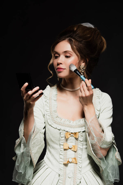 pretty woman in elegant vintage outfit applying face powder isolated on black - Fotografie, Obrázek