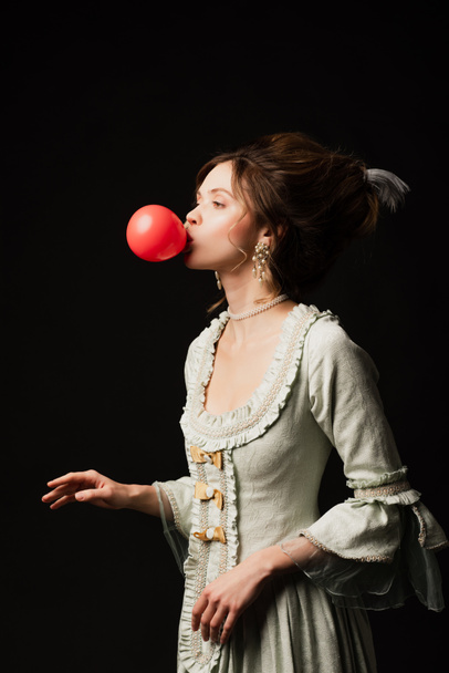 young woman in elegant vintage dress blowing chewing gum isolated on black - Photo, Image
