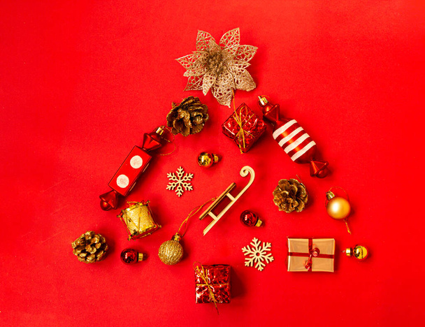Composición plana con un árbol de Navidad hecho de diferentes artículos festivos, copos de nieve, regalos, dulces, decoraciones de árboles de Navidad sobre un fondo rojo. Copiar espacio - Foto, Imagen