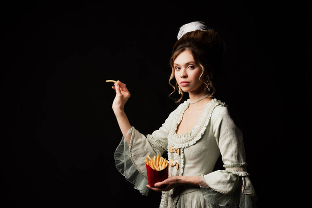 чарівна жінка в старовинній пастельній сірій сукні позує з картоплею фрі ізольовано на чорному
 - Фото, зображення