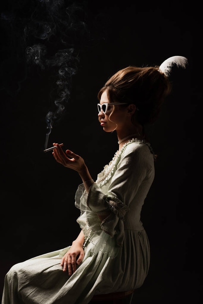 side view of vintage style woman in pastel grey dress smoking isolated on black - Fotoğraf, Görsel